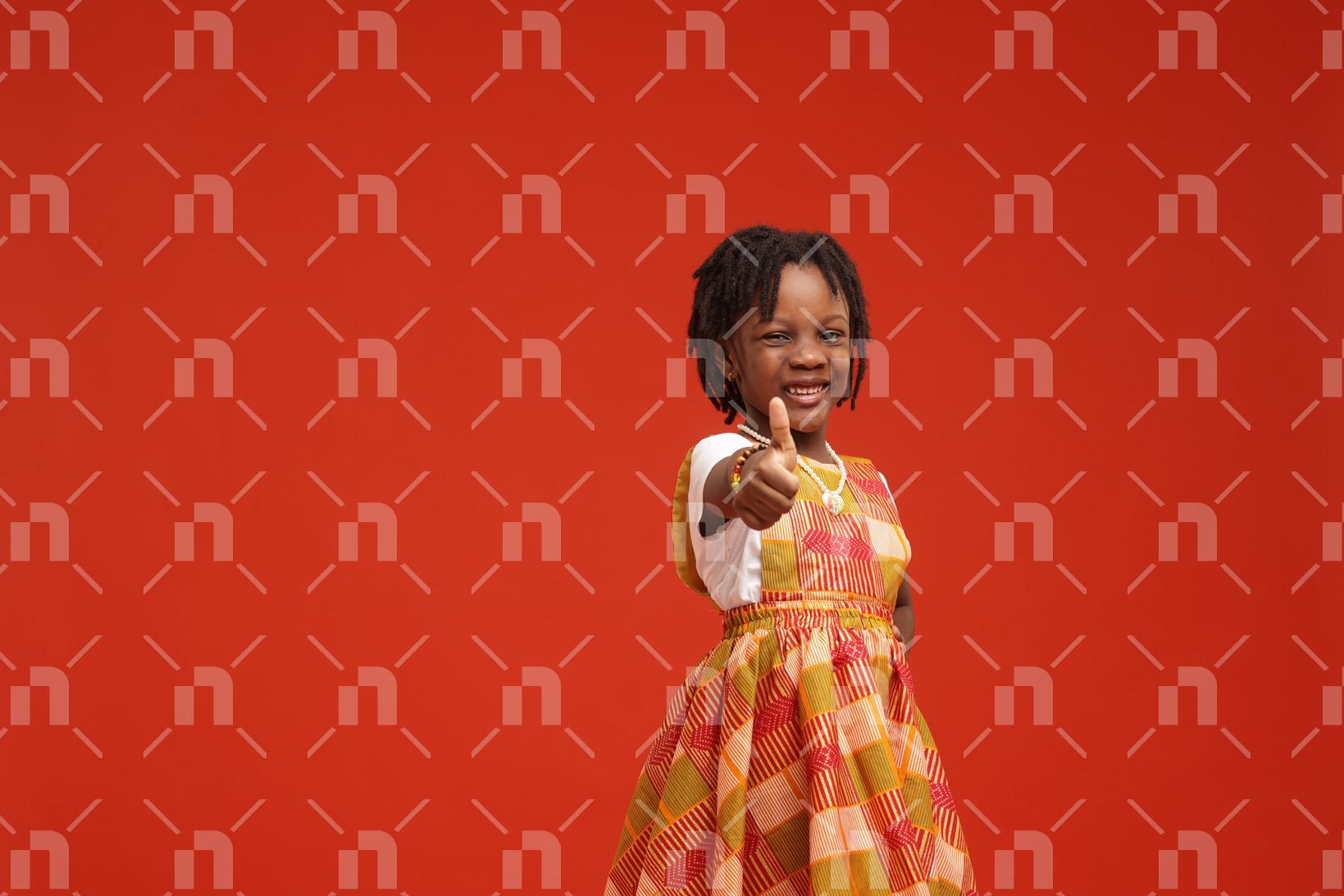 fillette-africaine-vetue-dune-robe-orange-posant-pour-une-photo-studio-en-montrant-le-pouce-droit-avec-le-sourire