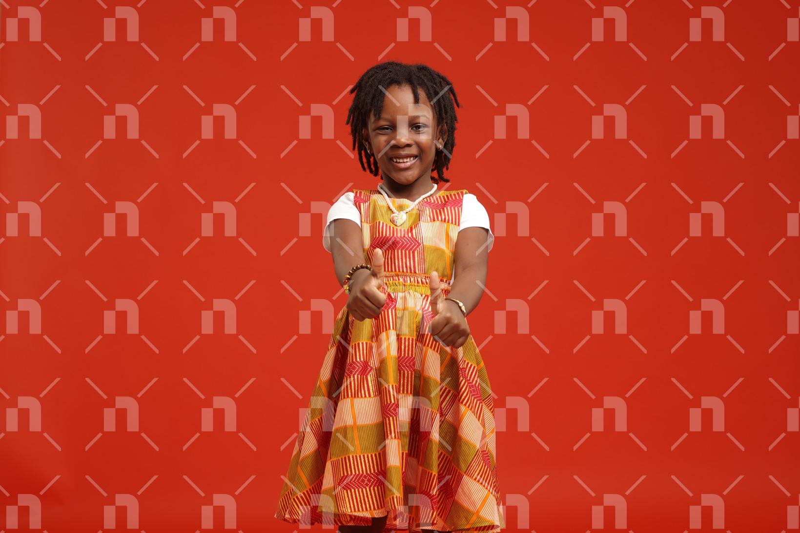 fillette-africaine-vetue-dune-robe-orange-posant-pour-en-photo-studio-les-deux-pouces-leves-avec-un-le-sourire