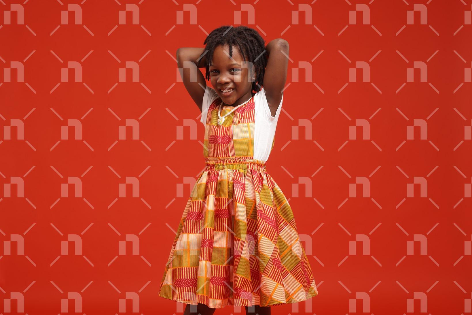 fillette-africaine-moderne-vetue-dune-robe-faite-en-pagne-de-couleur-orangedans-une-posture-avec-les-bras-croises-derriere-la-cou-pour-le-besoin-dune-photo-studio-avec-un-le-sourire