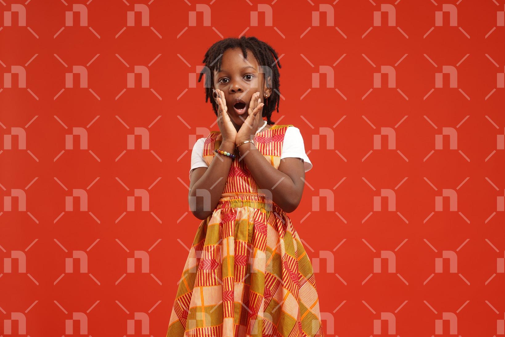 fillette-africaine-moderne-vetue-dune-robe-de-couleur-orange-posant-avec-les-mains-jointes-autour-de-la-bouche-et-les-yeux-grands-ouverts-en-signe-detonnement-pour-une-photo-studio