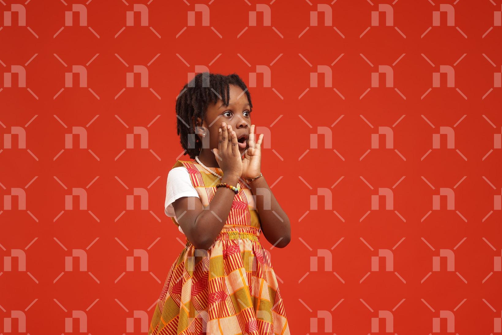 petite-fille-africaine-moderne-vetue-dune-robe-de-couleur-orange-executant-un-signe-detonnement-avec-la-bouche-et-les-yeux-grands-ouverts-pour-une-photo-studio