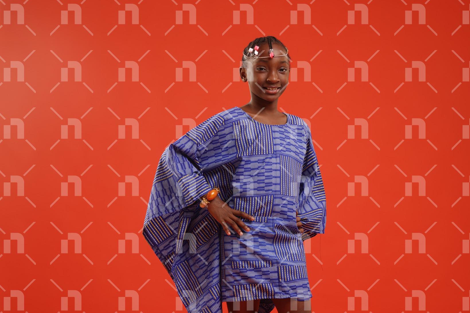 fillette-africaine-moderne-vetue-dune-robe-de-couleur-bleu-posant-legerement-de-profil-avec-les-deux-mains-a-la-hanche-et-un-grand-sourire-pour-une-photo-studio