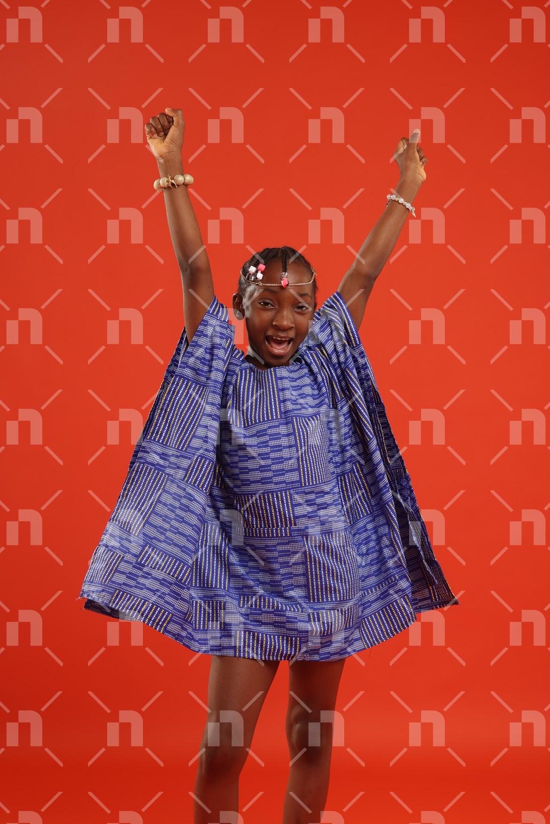 fillette-africaine-moderne-vetue-dune-robe-de-couleur-bleu-posant-les-deux-points-leve-avec-un-grand-sourire-pour-une-photo-studio