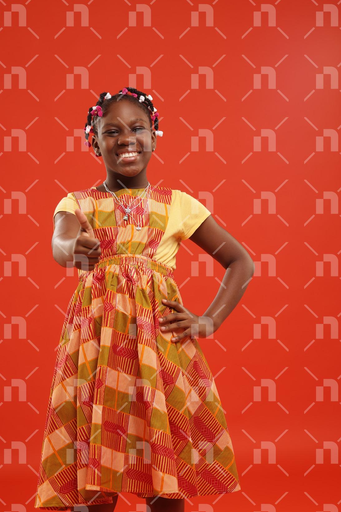fillette-africaine-moderne-vetue-dune-robe-de-couleur-orange-posant-le-pouce-droit-leve-et-un-sourire-pour-une-photo-studio