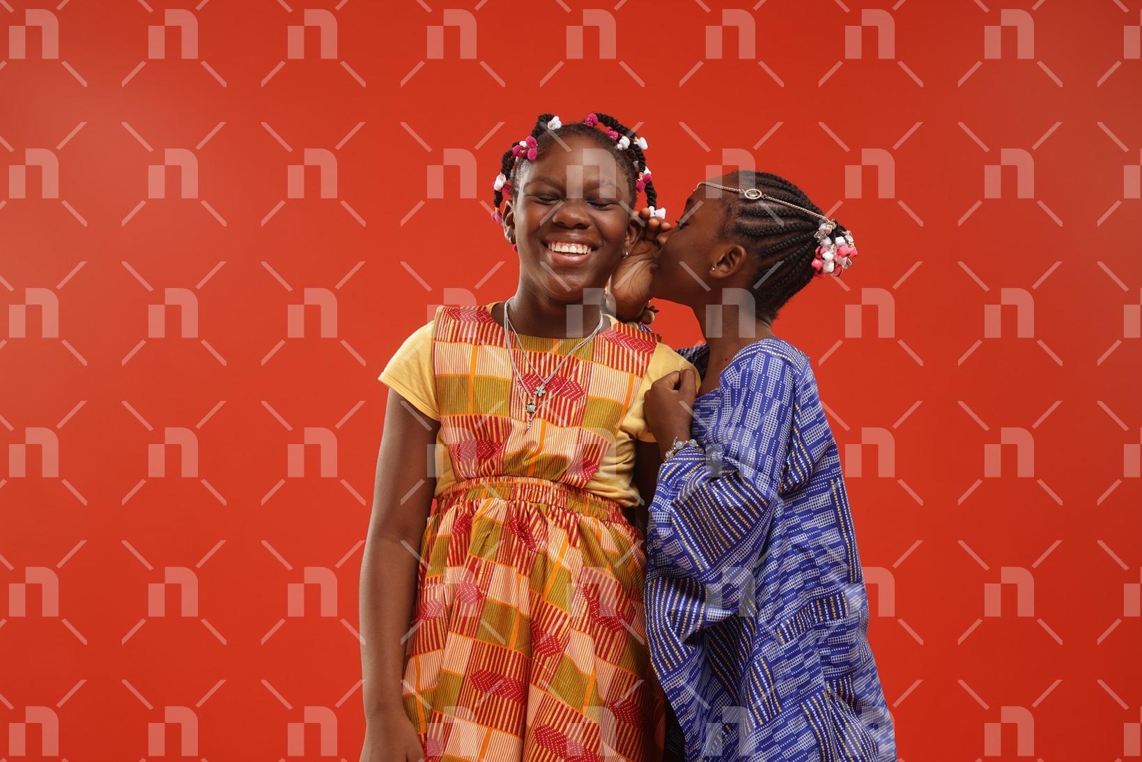 deux-filles-espiegles-en-tenue-de-ville-faite-de-pagne-traditionnel-dont-lune-chuchotant-a-loreille-de-son-amie-avec-le-sourire