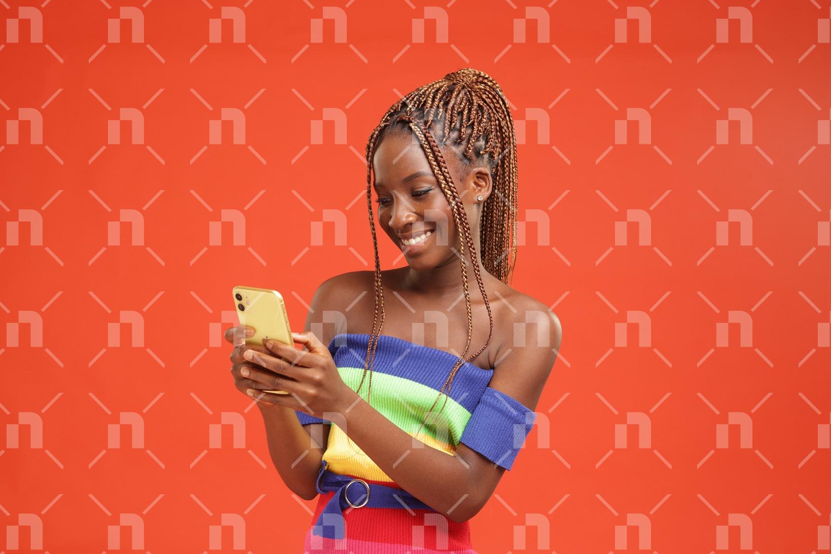 tenant-son-telephone-des-deux-mains-une-jeune-fille-africaine-moderne-pose-avec-le-sourire-en-regardant-lecran-de-son-telephone-portable