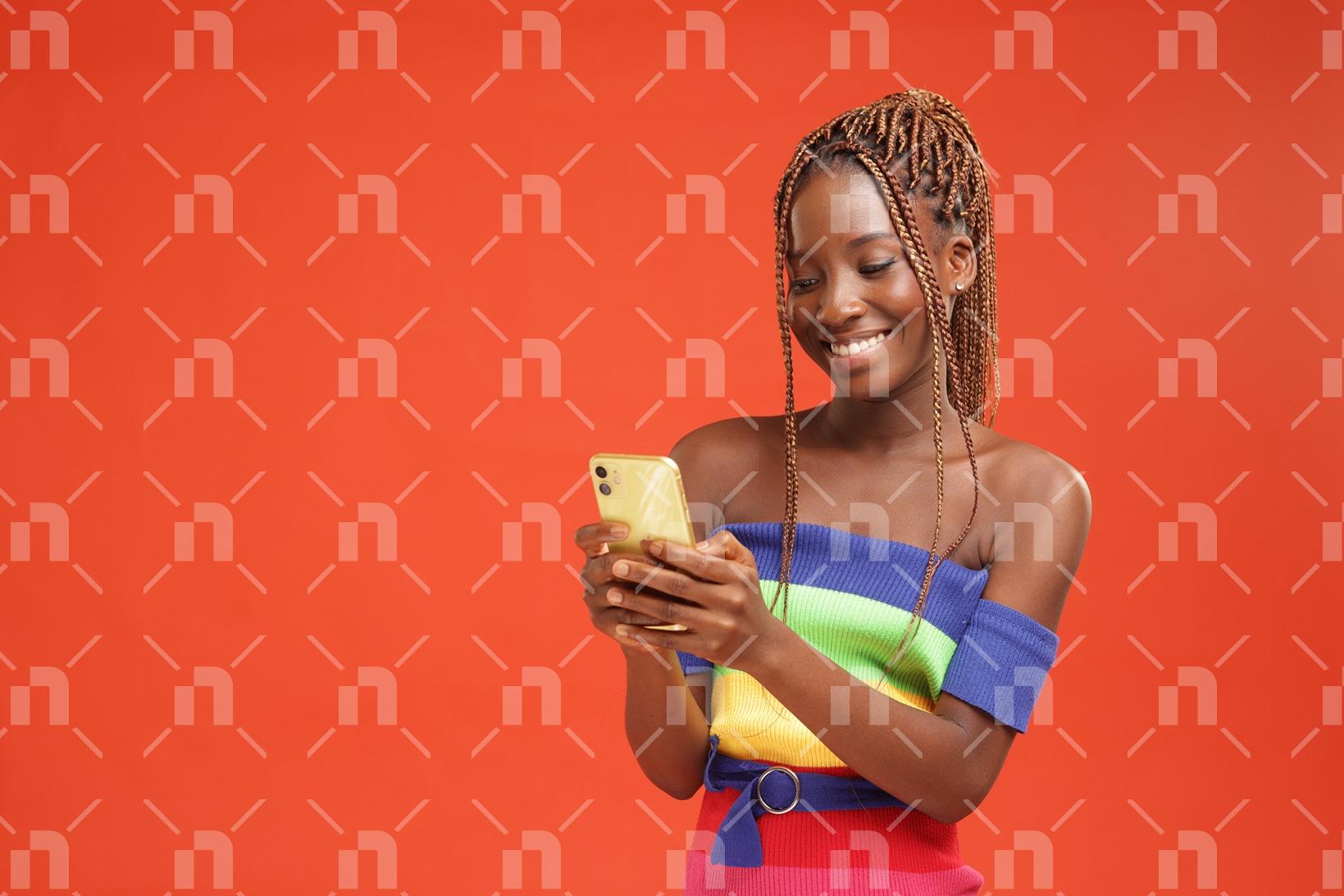 belle-jeune-fille-africaine-moderne-vetue-dune-robe-coloree-observant-son-telephone-un-fond-orange