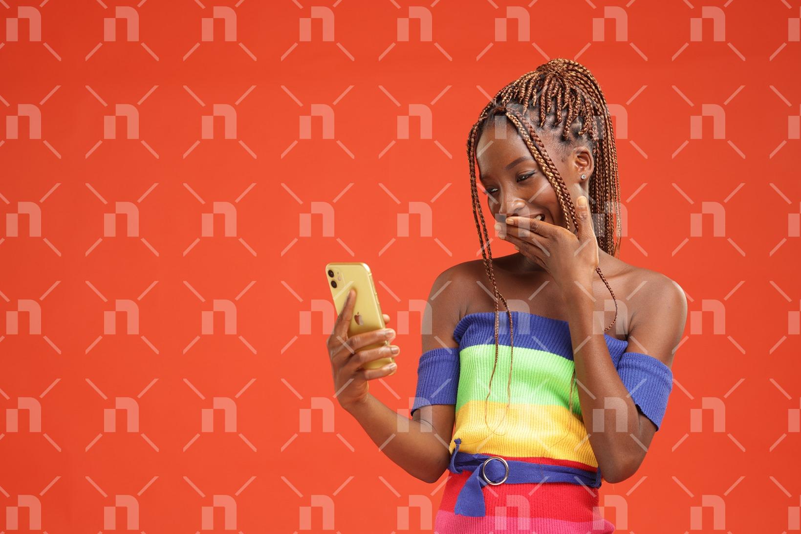 en-robe-decolletee-couleur-arc-en-ciel-jeune-fille-africaine-heureuse-de-parcourir-son-smartphone-en-se-cachant-le-sourire-avec-la-main-gauche-pour-photo-studio