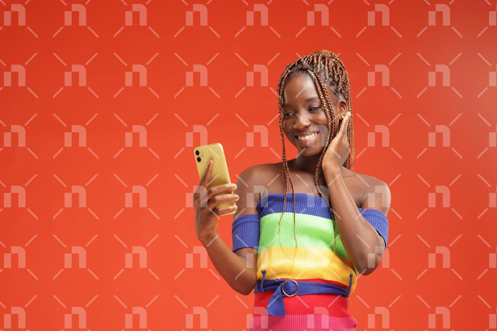 jeune-fille-africaine-moderne-vetue-dune-robe-coloree-pose-pour-photo-studio-en-souriant-et-en-posant-le-regard-sur-son-telephone