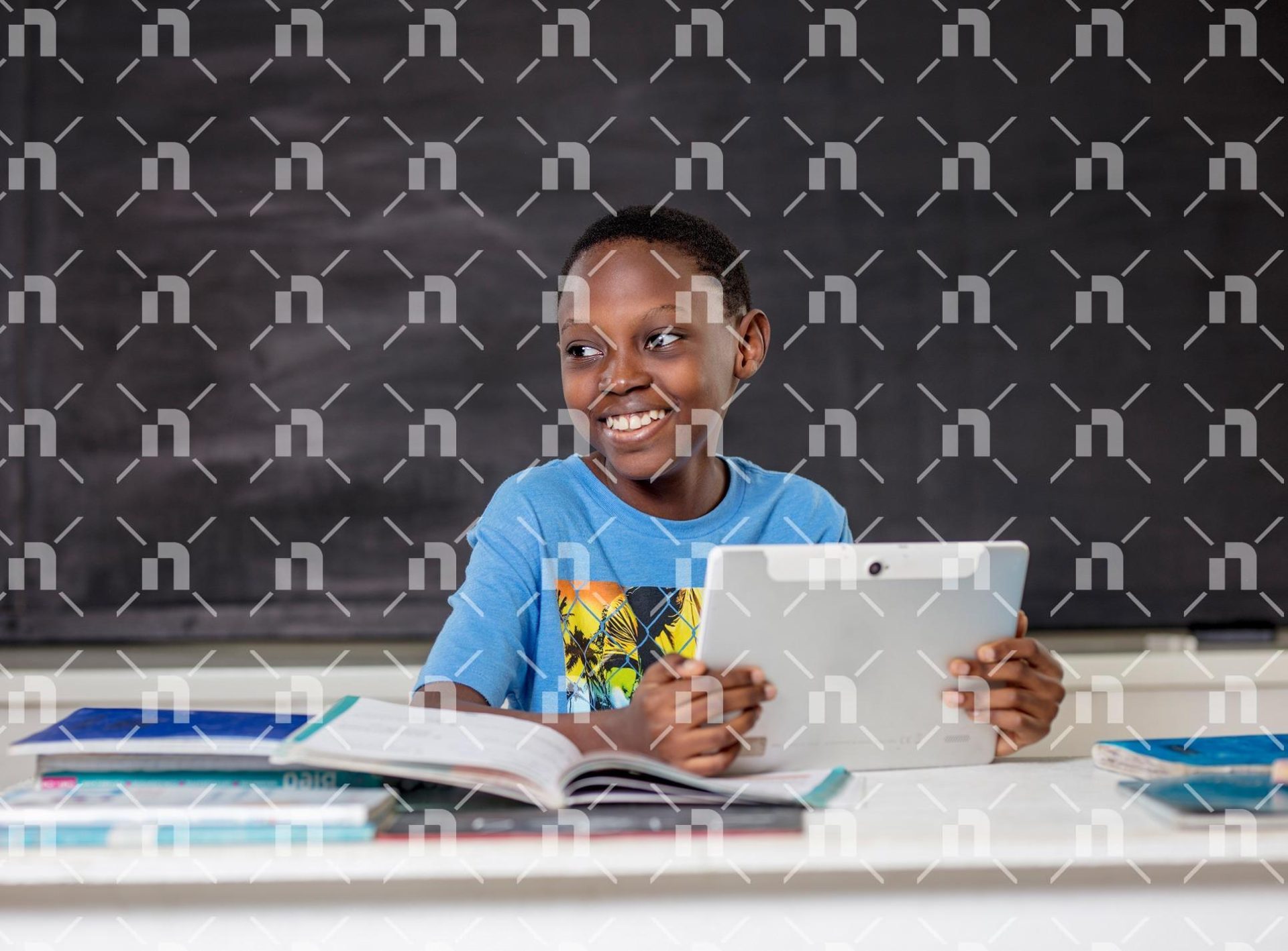 un-enfant-en-t-shirt-tenant-une-tablette-avec-le-sourire-et-le-regard-ailleurs-dans-une-salle-de-classe