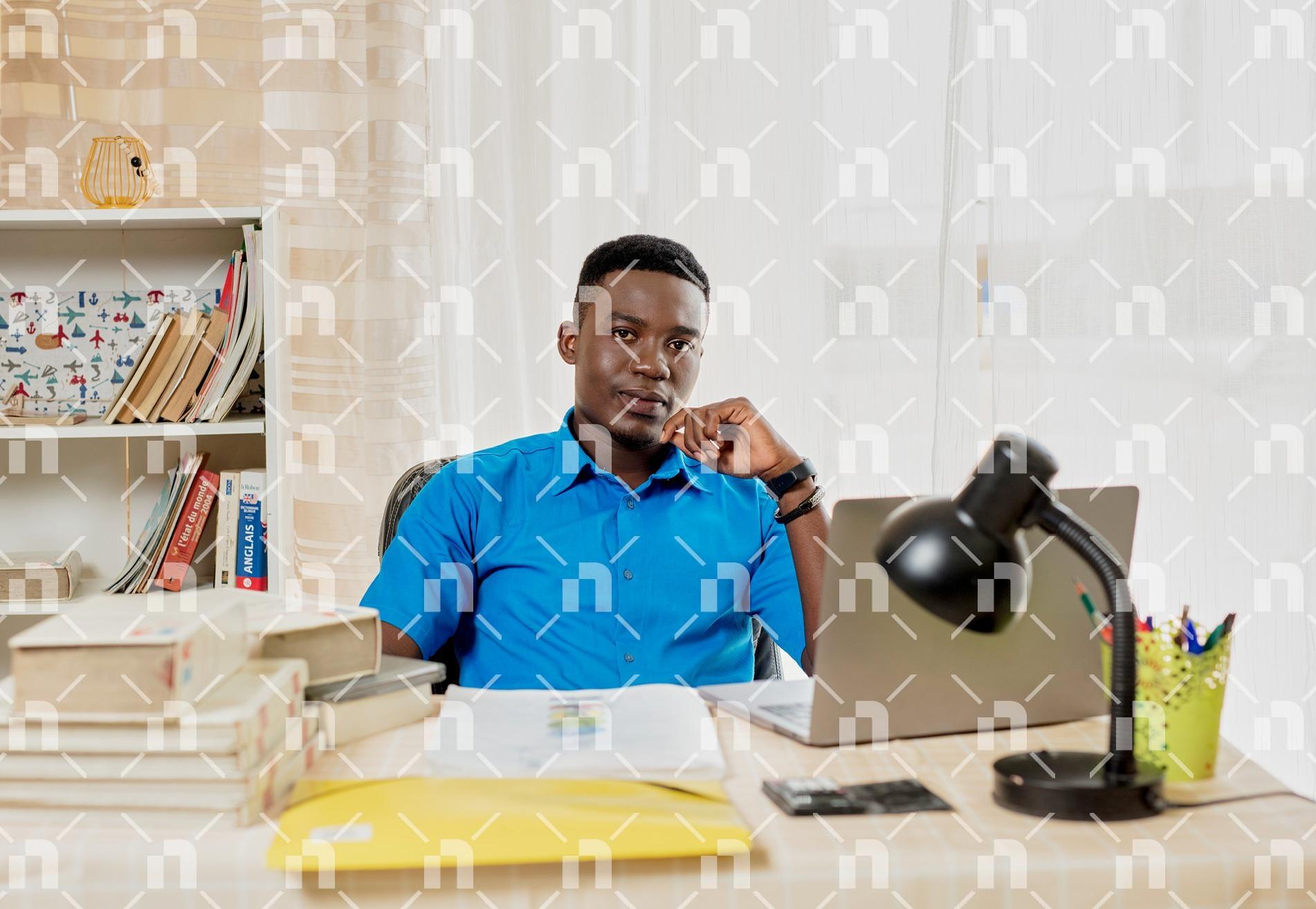 homme-de-teint-noir-assis-dans-un-bureau-en-face-de-son-ordinateur-avec-une-table-pleine-de-livres-et-de-cahiers