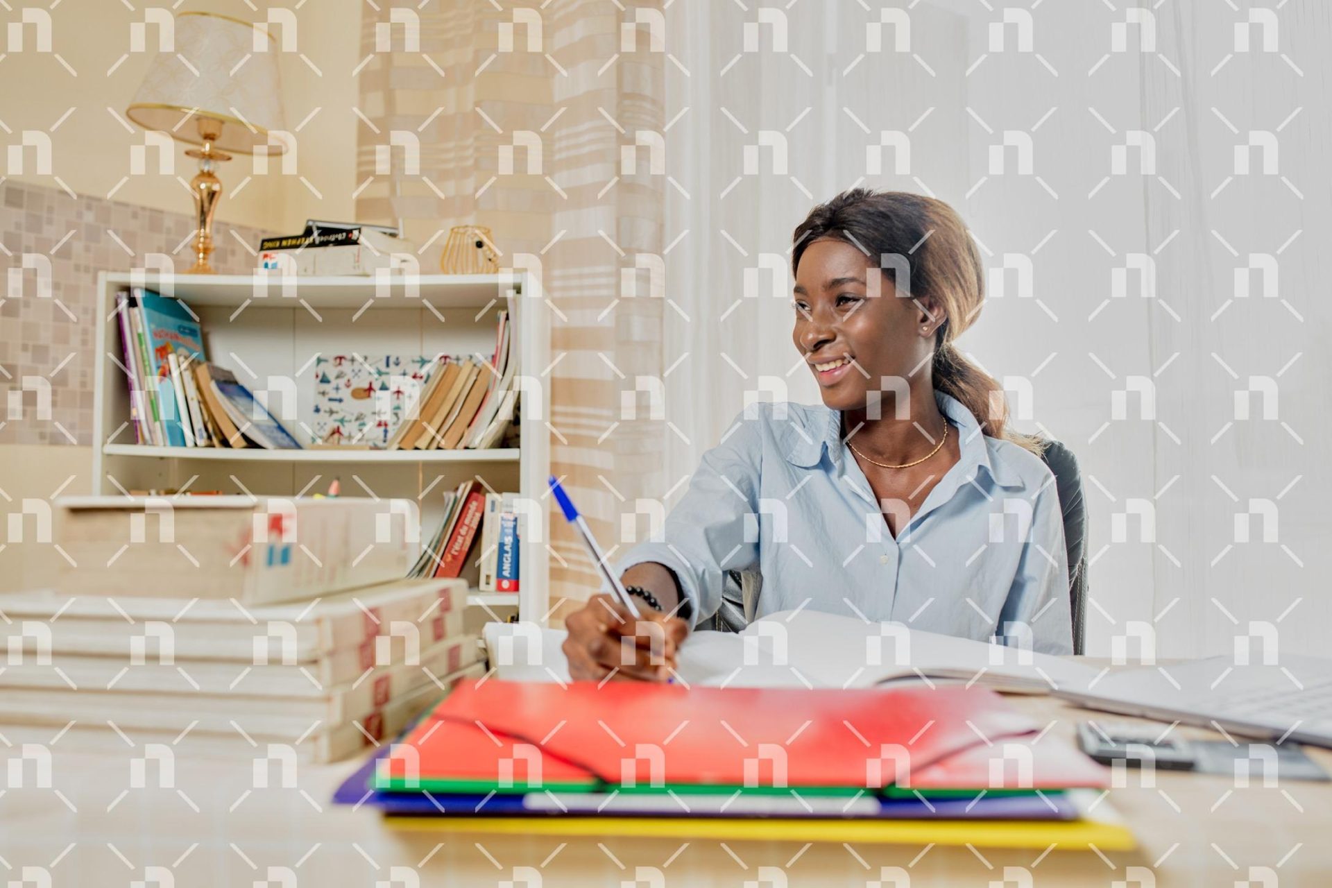 une-jeune-femme-africaine-souriante-tournee-vers-la-droite-en-train-decrire-dans-un-grand-cahier-a-son-bureau-avec-un-ordinateur-portable-a-ses-cotes
