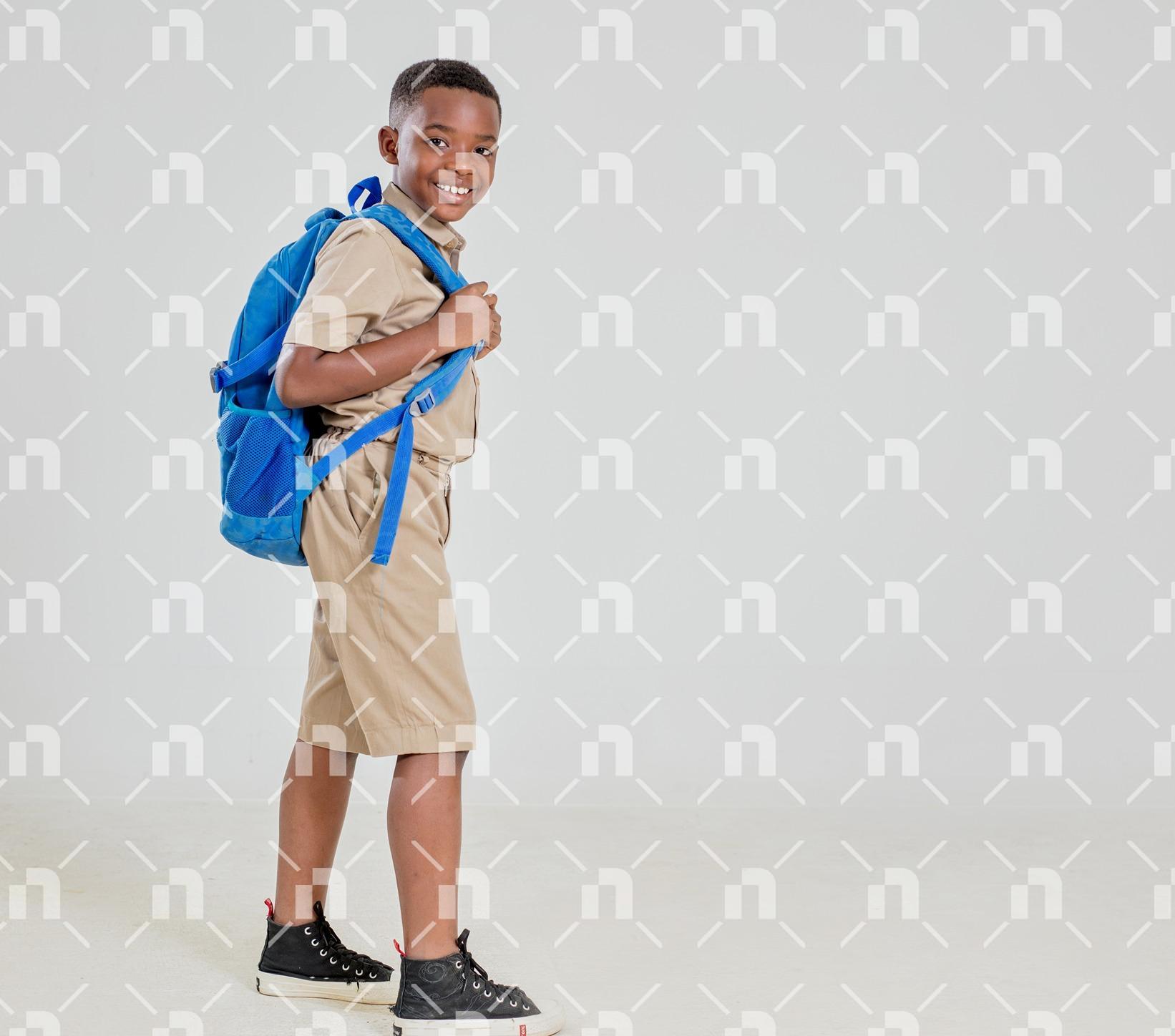 jeune-garcon-africain-souriant-en-tenue-decole-kaki-posant-avec-un-sac-a-dos-sur-un-fond-neutre