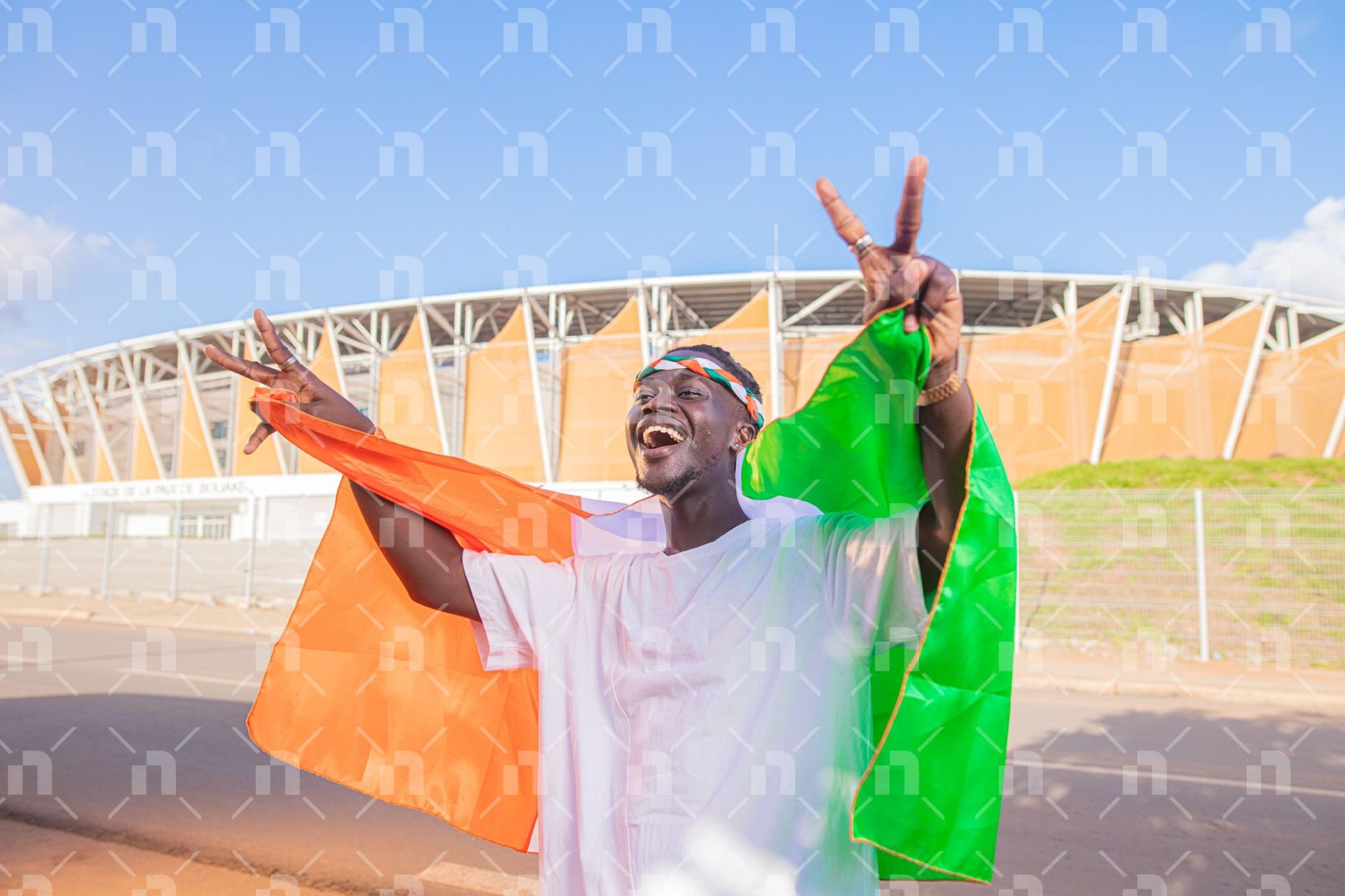 supporteur-ivoirien-tenant-le-drapeau-avec-les-deux-doigts-en-lair-derriere-le-stade